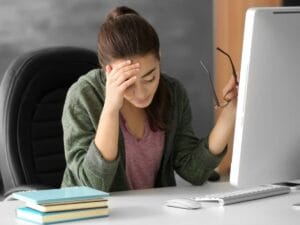 Zasmucona kobieta przy komputerze, podpiera ręką głowe.