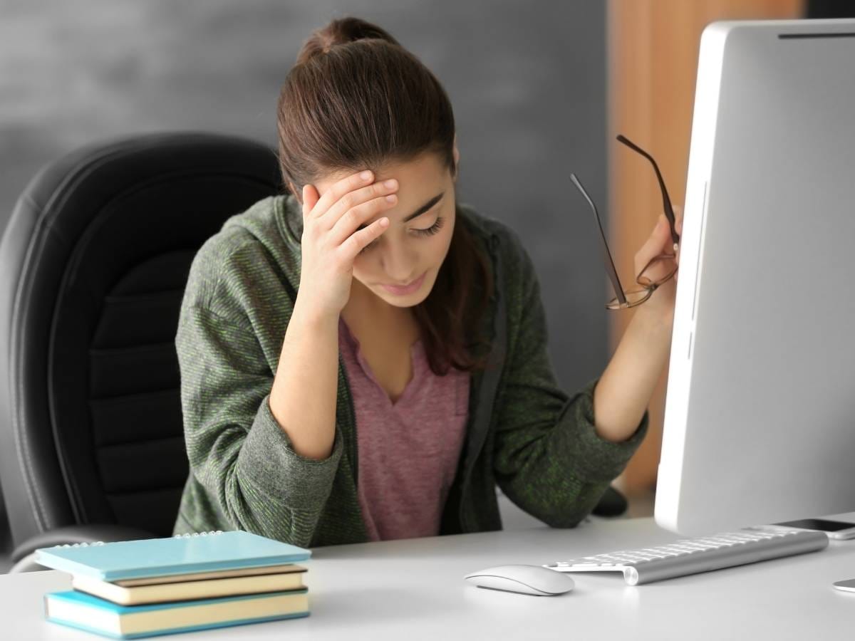 Zasmucona kobieta przy komputerze, podpiera ręką głowe.