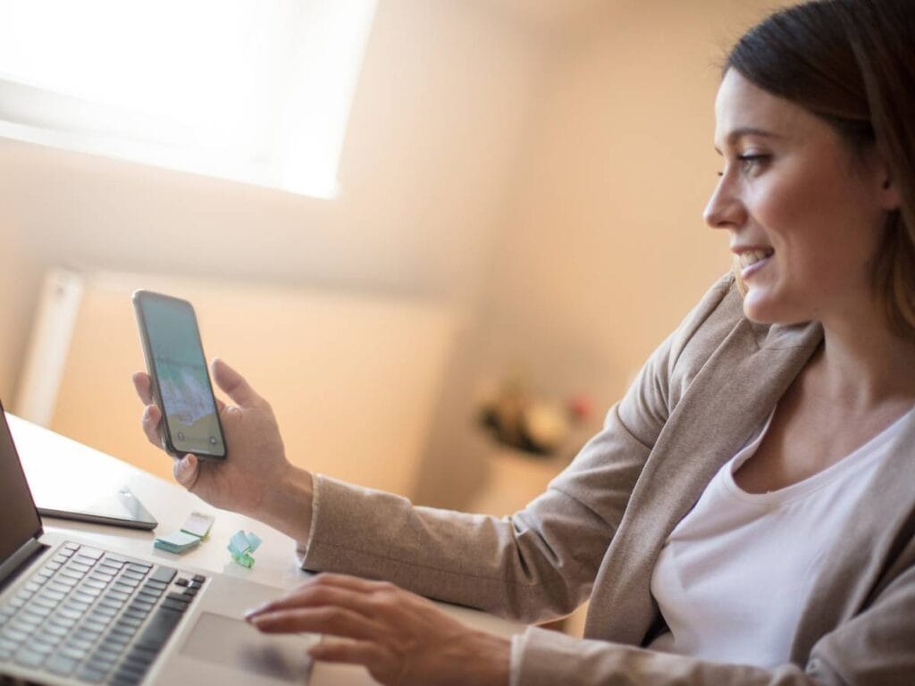 Kobieta z telefonem, patrzy w ekran i uśmiecha się