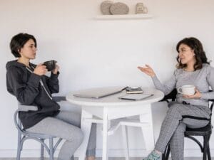 Dwie kobiety w swobodnej rozmowie przy stole.