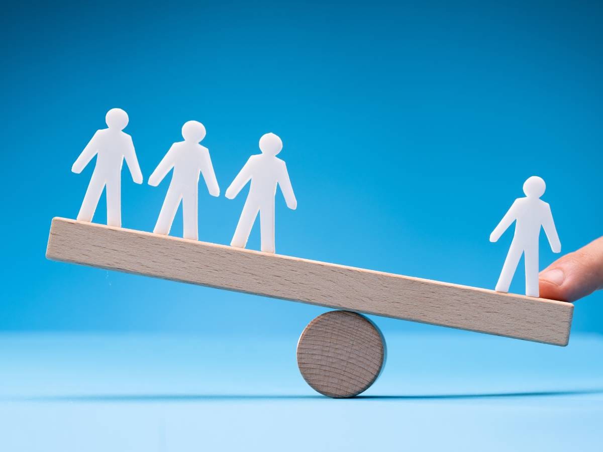 Rysunek huśtawki i postaci na niej , gdzie trzy są mniej ciężkie niż jedna sylwetka i palec.