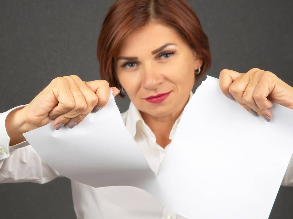 Kobieta w białej bluzce rozrywa dokumenty.