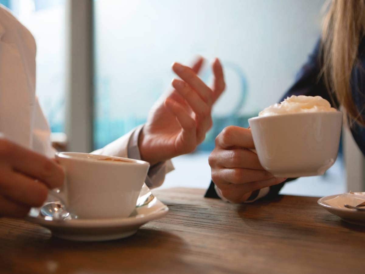 Zbliżenie na ręce ludzi w czasie rozmowy przy filiżance kawy.