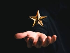 Dłoń wyłaniająca się z ciemności i złota gwiazdka nad nią.