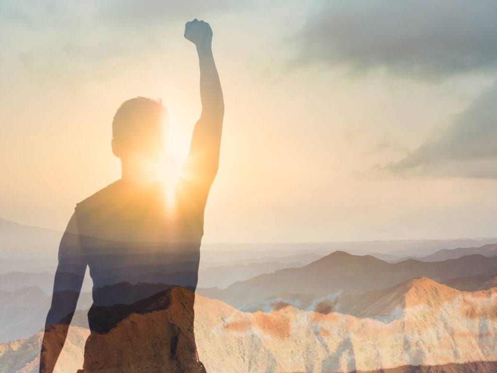 Mężczyzna z uniesioną ręka na tle słońca